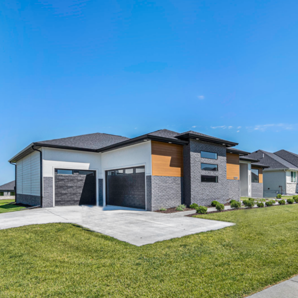 A modern custom-built home featuring a sleek combination of black brick, white stucco, and warm wood paneling.