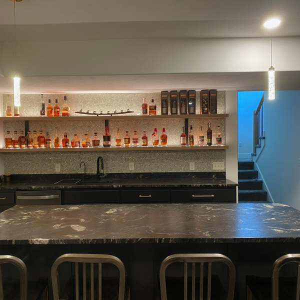 Custom-built home bar with black marble countertops, open shelving, and under-shelf lighting.