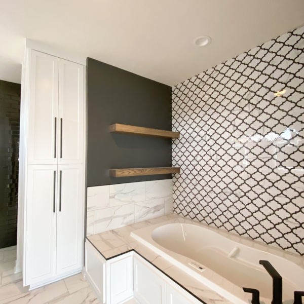 Master bathroom with geometric tile walls, built-in soaking tub, and modern floating shelves.