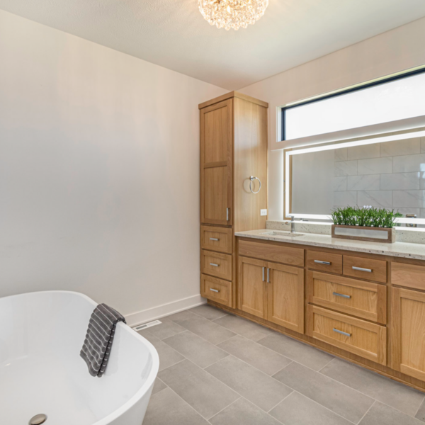 A spa-like bathroom featuring a freestanding soaking tub, custom wood cabinetry, and a large illuminated mirror.