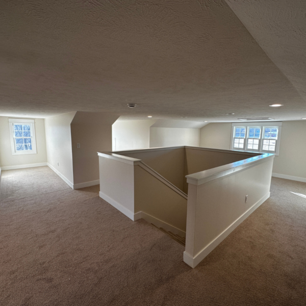 Open-concept carpeted loft space with white trim and natural light.