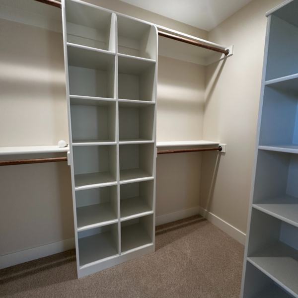 Walk-in closet with white custom shelving and wooden hanging rods.