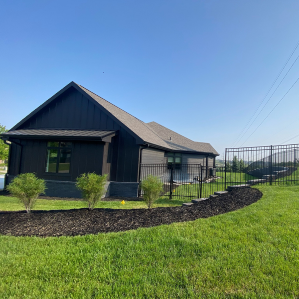 Backyard view of a custom home in Elkhorn, NE, featuring dark wood siding, a fenced yard, and manicured landscaping.