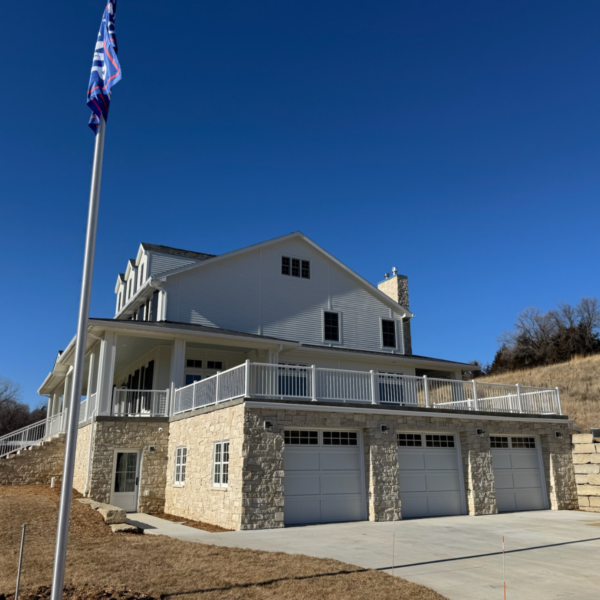 Rear view of a farmhouse with a wraparound deck and three-car garage