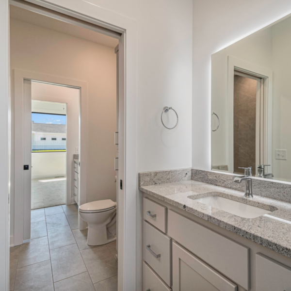 A sleek bathroom with a granite countertop double vanity, white cabinetry, and a large mirror.