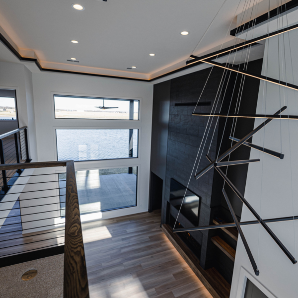 Modern loft overlooking a great room, featuring metal railings, large windows, and a geometric chandelier.