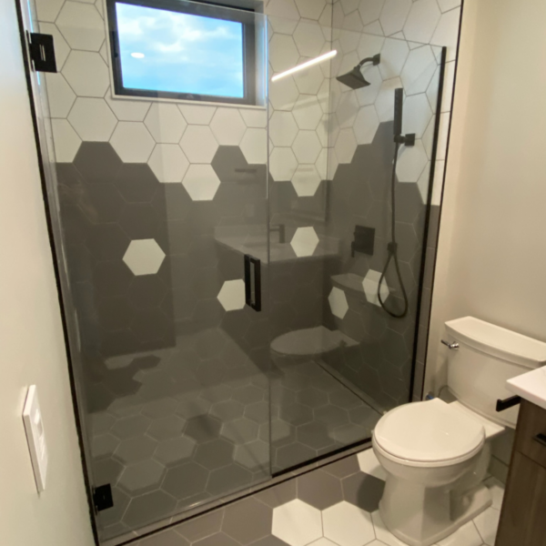 Modern bathroom with a bold black-and-white hexagon tile design and a glass-enclosed walk-in shower.