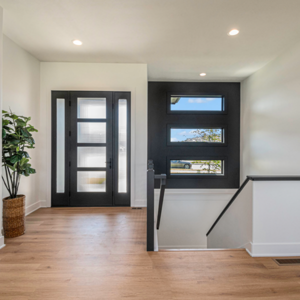 A modern entryway with a black front door, geometric windows, and a staircase leading to the lower level.