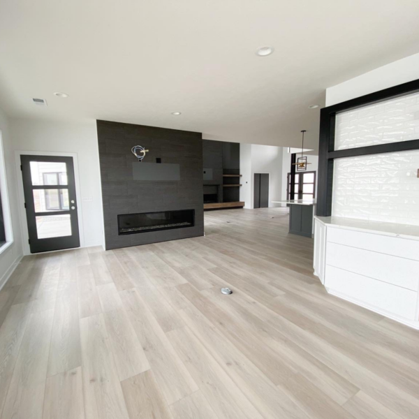 Modern open-concept living space with a black feature fireplace, light wood flooring, and sleek built-ins.