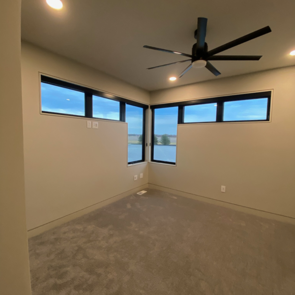 Spacious modern bedroom with a corner window and contemporary ceiling fan.