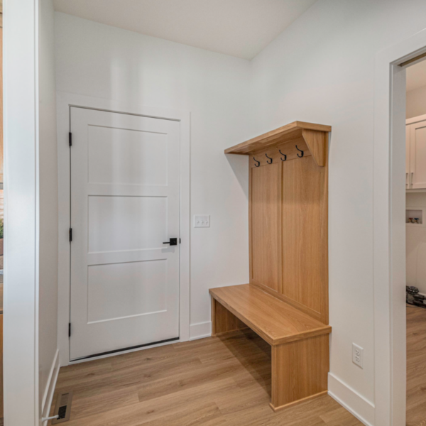 A functional mudroom with a built-in wooden bench, coat hooks, and white walls.