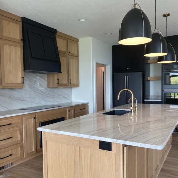 Elegant kitchen island with marble countertops, gold faucet, and modern black pendant lighting.