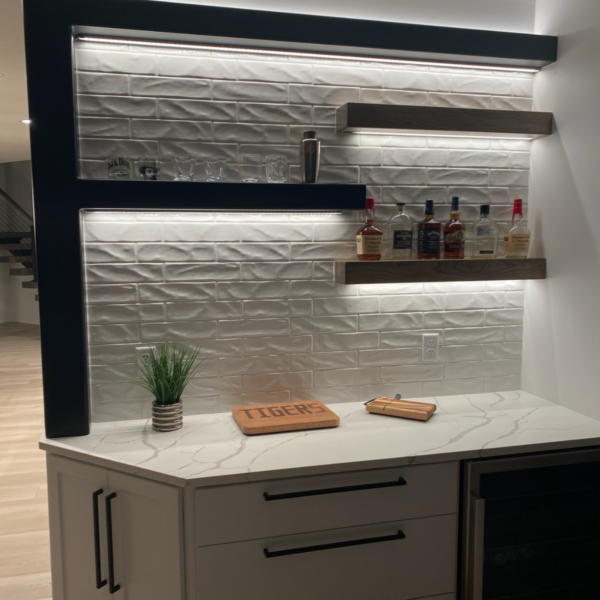 Built-in home bar with LED lighting, modern floating shelves, and a sleek white backsplash.