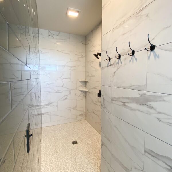 Large walk-in shower with marble tile walls, pebble flooring, and black hardware.