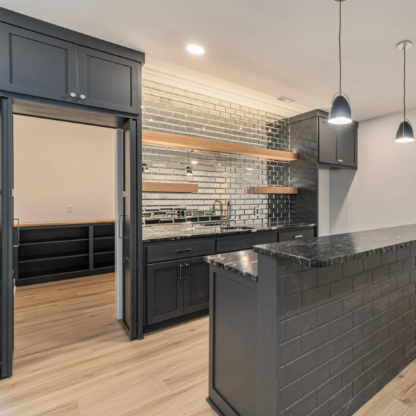 A stylish home bar featuring black cabinetry, a mirrored backsplash, and modern lighting.